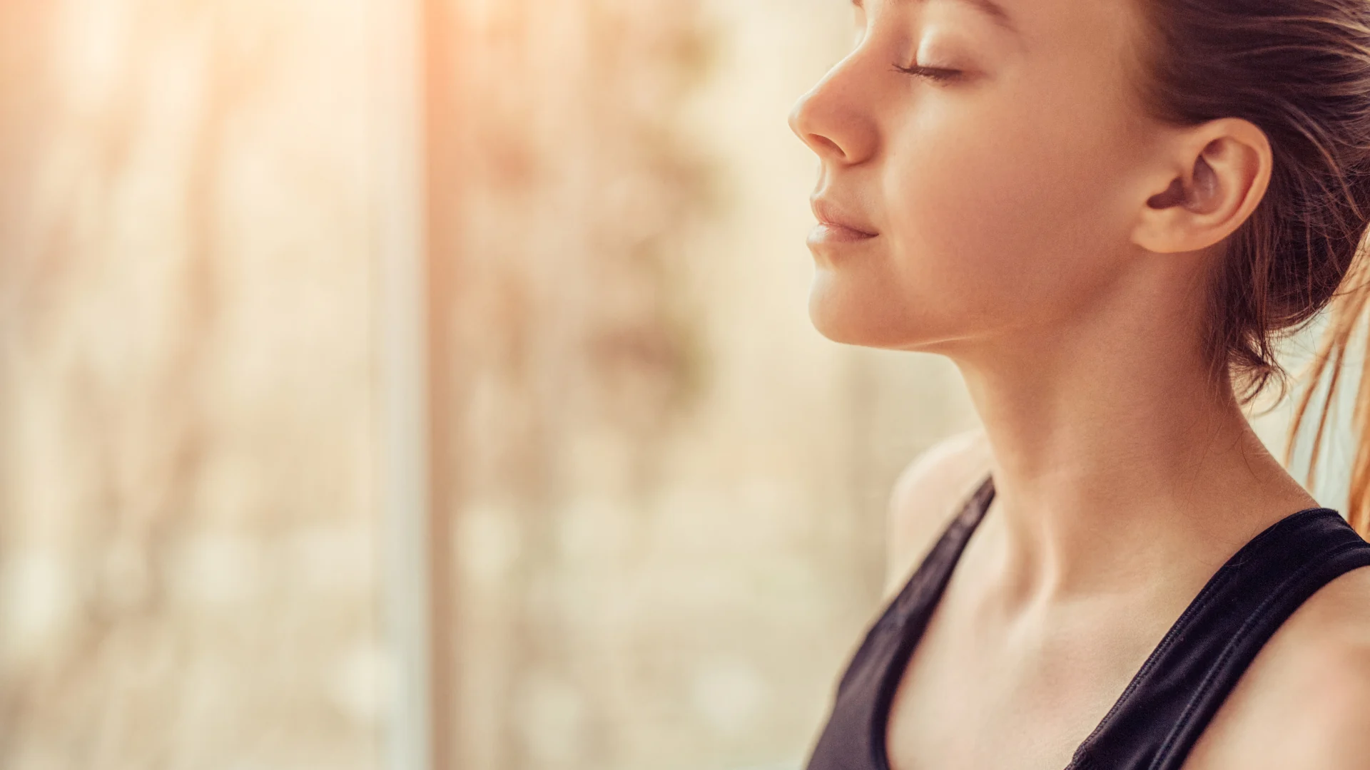 Femme les yeux fermés près d’une fenêtre
